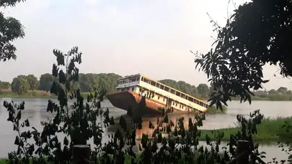 A collapsed bridge sinking into a calm green river, framed by dark trees.