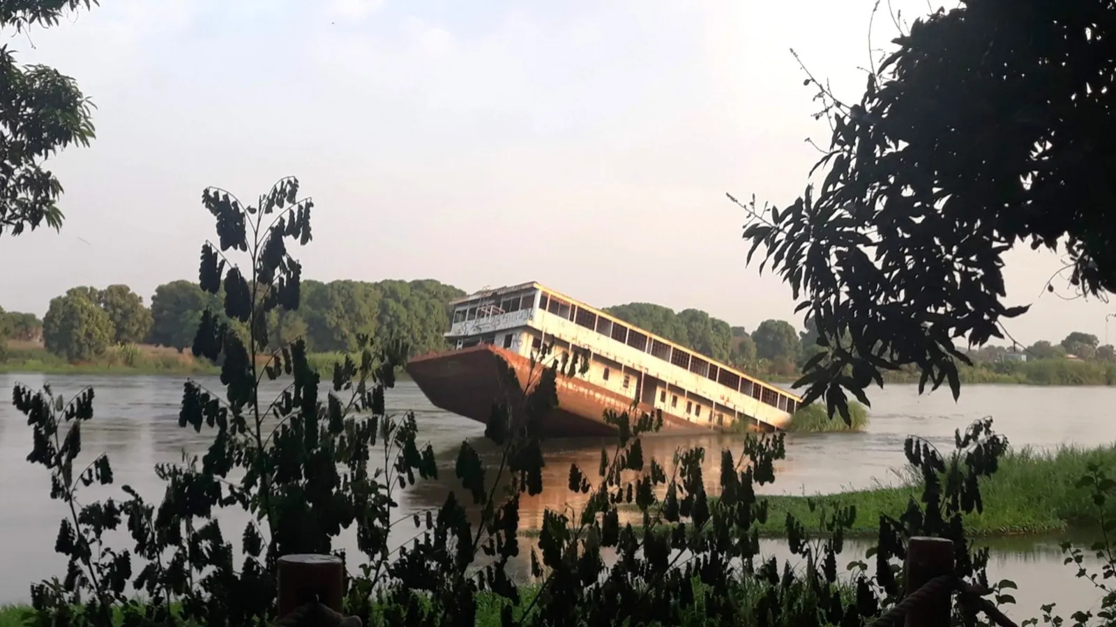 A collapsed bridge sinking into a calm green river, framed by dark trees.